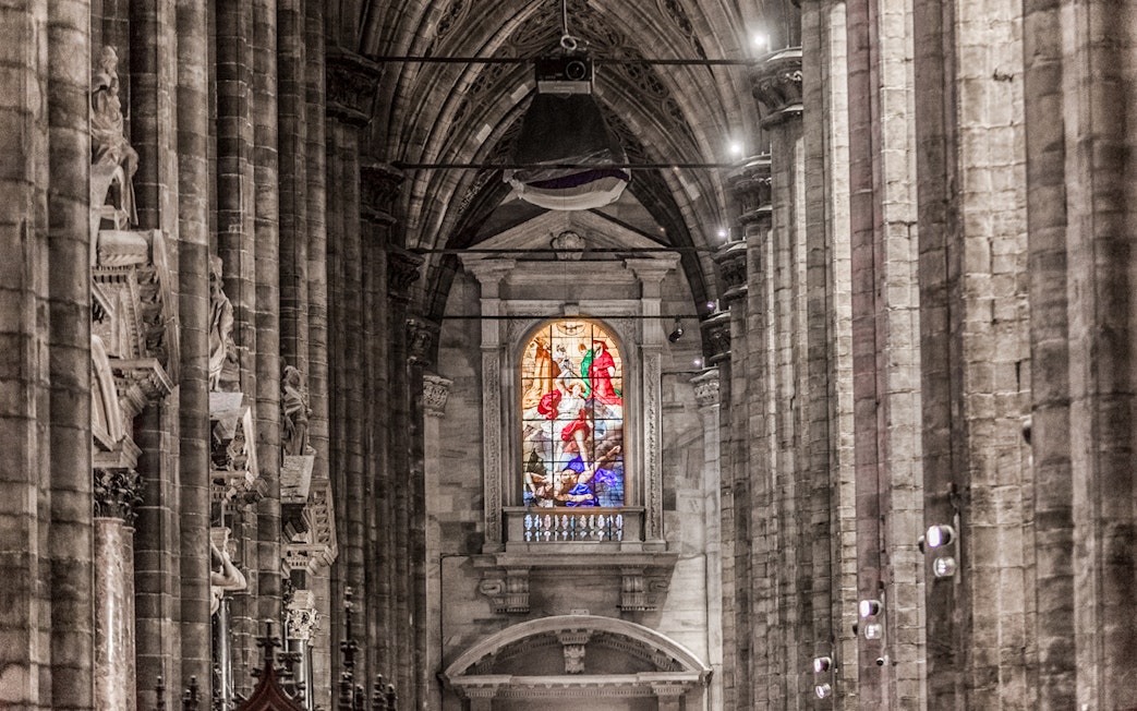 Stained glass window and stone columns inside Duomo Cathedral, Milan.