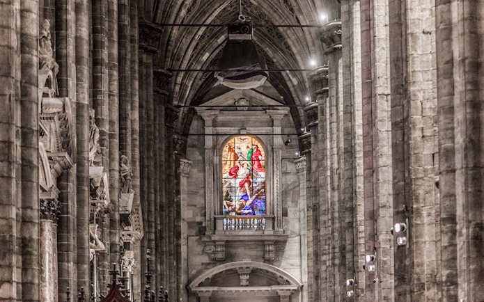 Stained glass window and stone columns inside Duomo Cathedral, Milan.