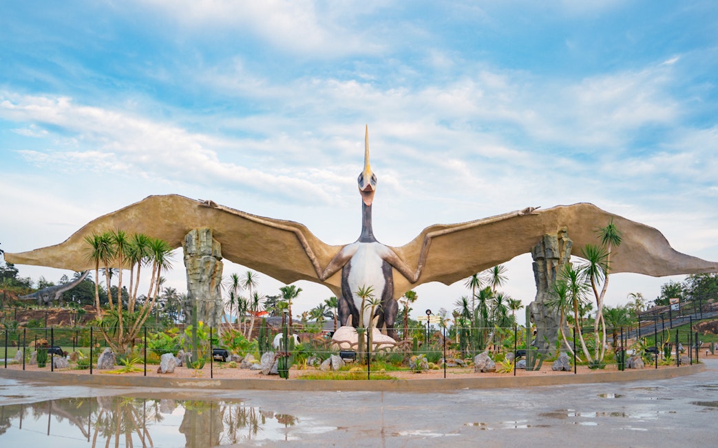 Pterosaur statue in Dino Desert park with surrounding palm trees.