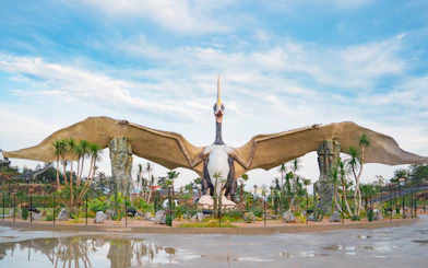 Pterosaur statue in Dino Desert park with surrounding palm trees.