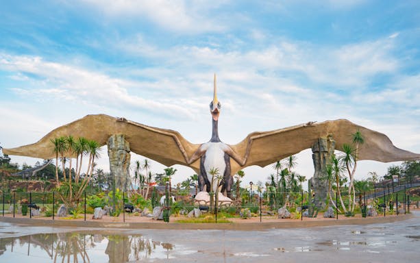Pterosaur statue in Dino Desert park with surrounding palm trees.