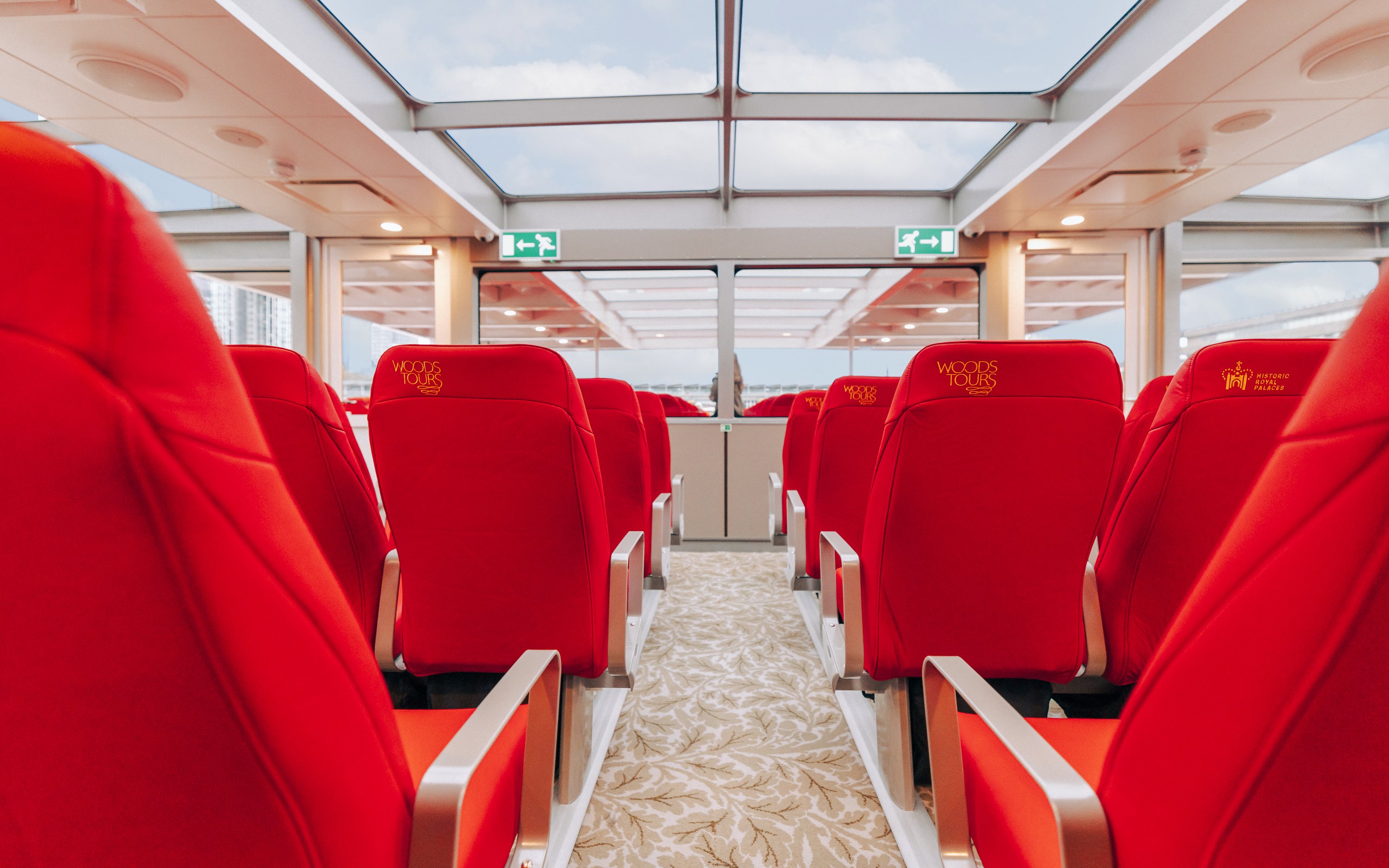 Interior seating of Tower of London Cruise boat with red chairs and glass ceiling.