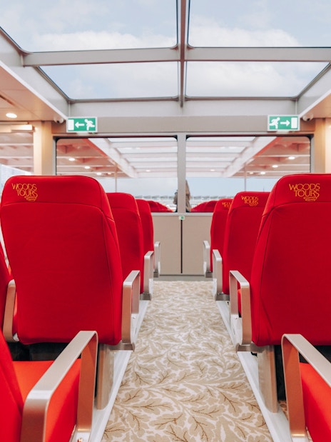 Interior seating of Tower of London Cruise boat with red chairs and glass ceiling.