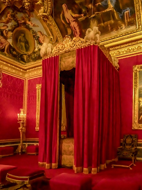 Palace of Versailles royal room with ornate bed canopy and chandeliers.