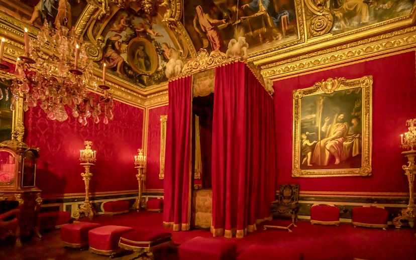 Palace of Versailles royal room with ornate bed canopy and chandeliers.