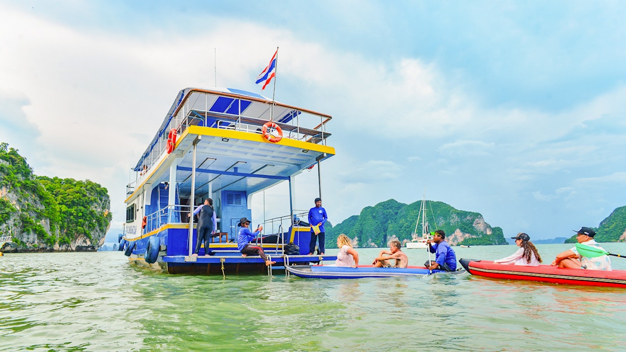 Tourists kayaking near a boat at Phang Nga Bay with limestone cliffs in the background.