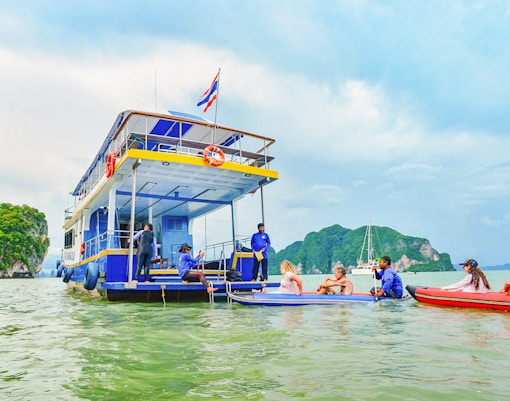 Tourists kayaking near a boat at Phang Nga Bay with limestone cliffs in the background.