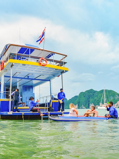 Tourists kayaking near a boat at Phang Nga Bay with limestone cliffs in the background.