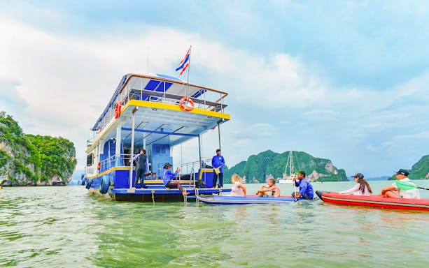 Tourists kayaking near a boat at Phang Nga Bay with limestone cliffs in the background.