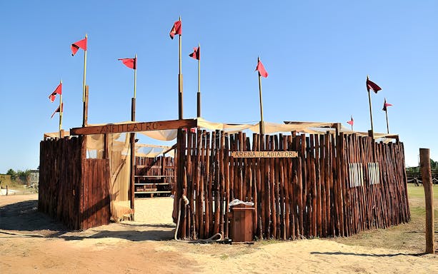 Reconstructed Roman arena at Roma World with wooden fencing and red flags.