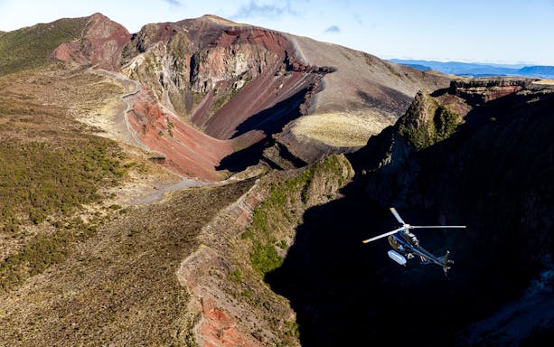 Helicopter flying over Mount Tarawera's volcanic landscape, showcasing rugged terrain and crater views.