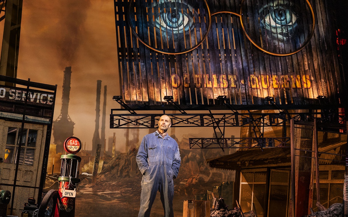 Man in overalls stands under billboard with eyes, set from The Great Gatsby.