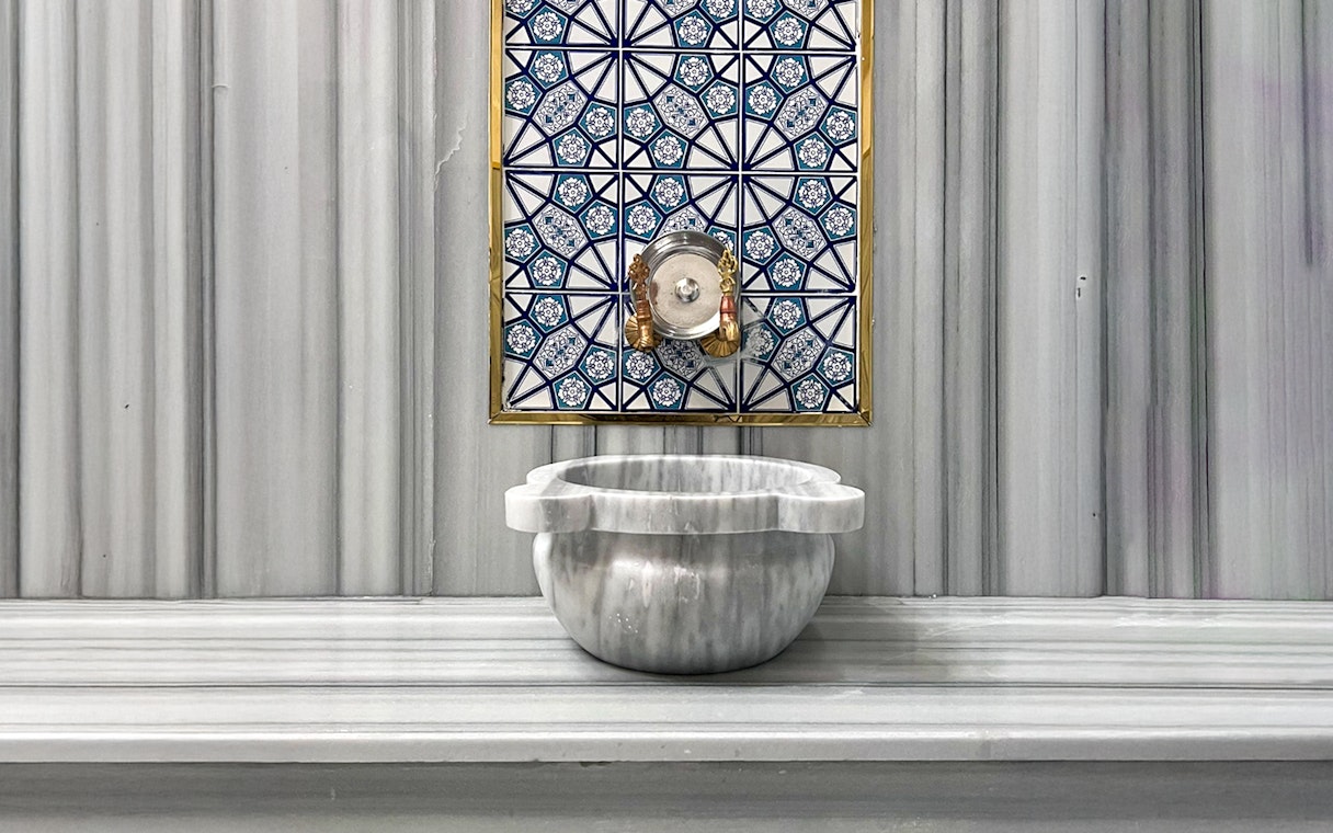 Marble basin and ornate tile wall inside Sifa Hamam.