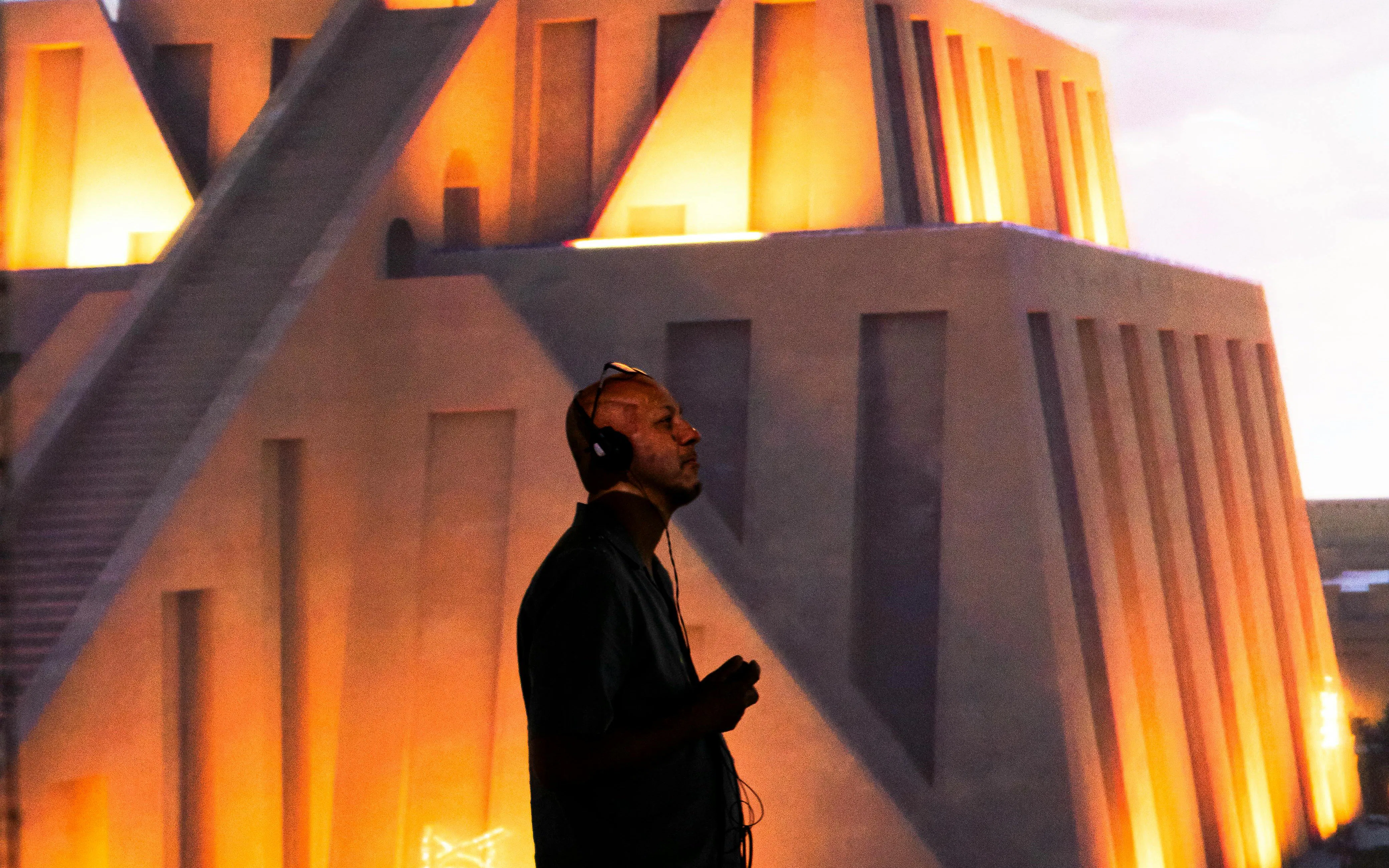 Man with headphones at London Timewalk Exhibition, illuminated ancient structure in background.
