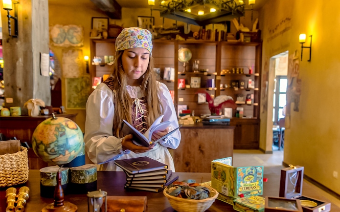 Performer in historical costume reading a book at Puy du Fou España park.