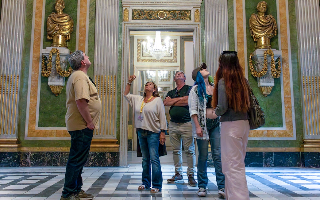 Visitors on a guided tour in the Picasso Museum, observing ornate sculptures and decor.