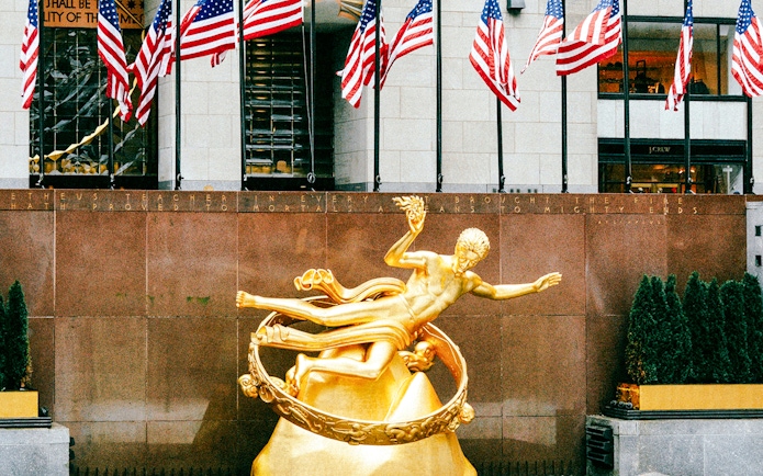 Prometheus Statue at Rockefeller Center with American flags in the background.