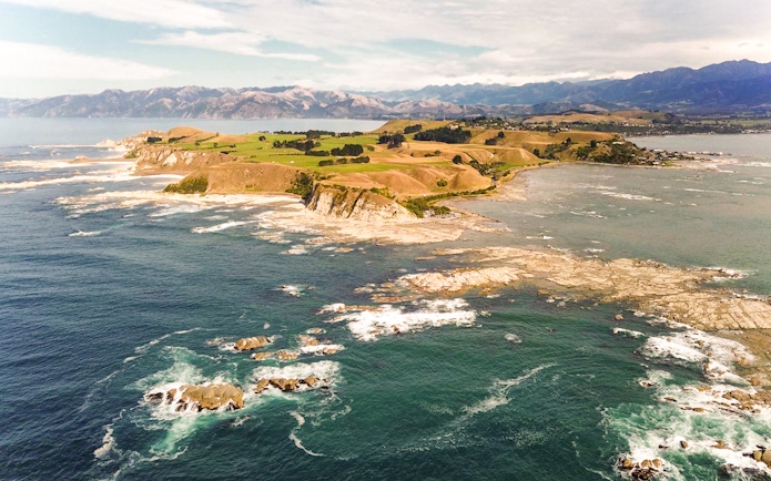 Aerial view of Kaikoura coastline with rocky shores and distant mountains.