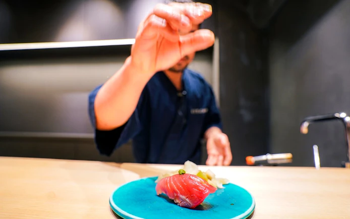 Sushi chef preparing tuna sashimi on a blue plate during Tokyo Omakase tour in Shinjuku.