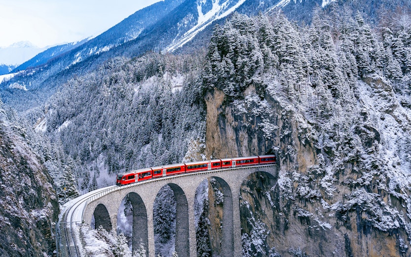Bernina Express crossing a snowy viaduct in the Swiss Alps.