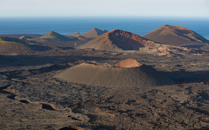 Volcanic landscape of Timanfaya National Park with ocean in the background.