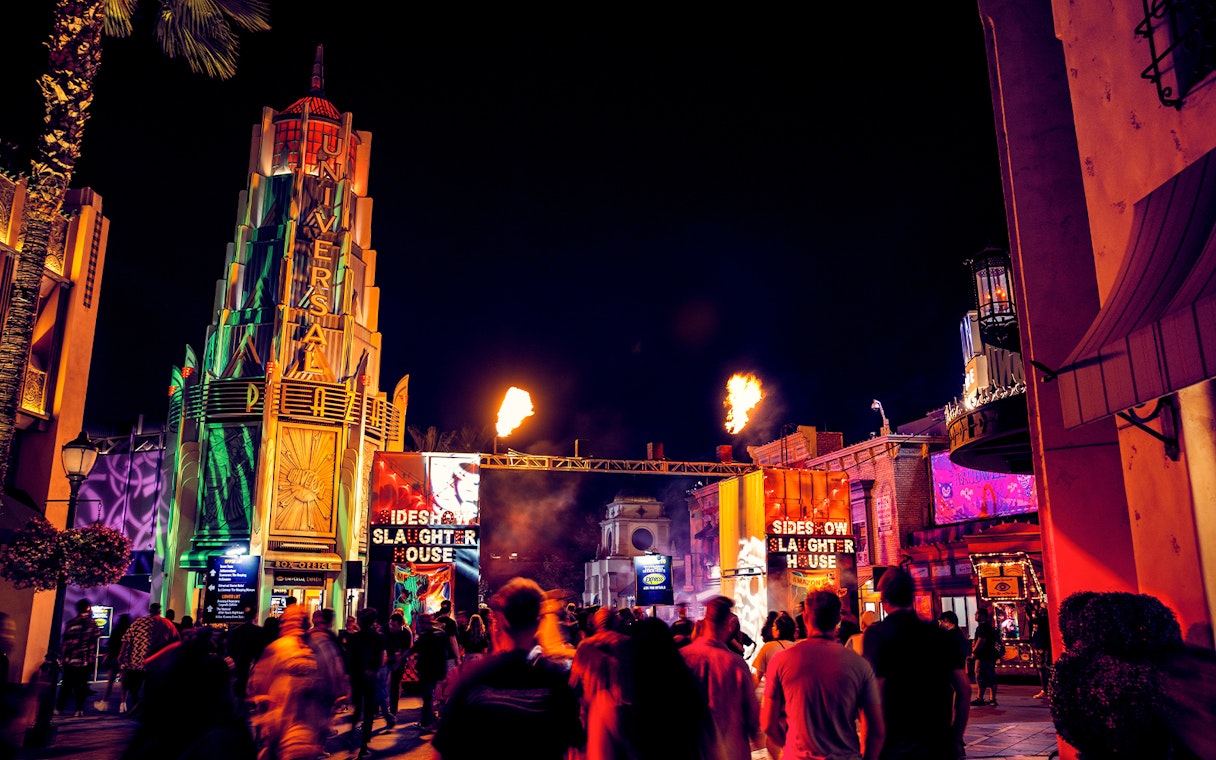 Crowds at Hollywood Horror Nights, Universal Studios Hollywood, with fiery entrance and neon lights.