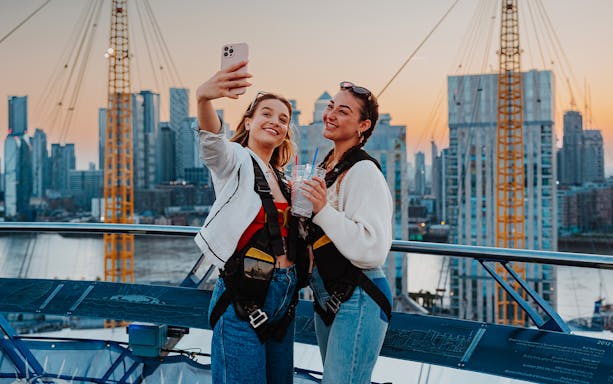 Guests taking a selfie atop the O2 with a city skyline at sunset.