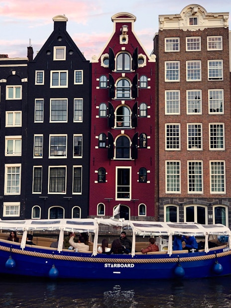 Covered canal cruise boat on Amsterdam canal with historic buildings in the background.