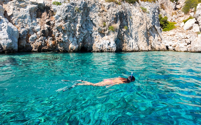 Woman snorkeling in turquoise waters near rocky cliffs during Majestic Catamaran Caldera Cruise.