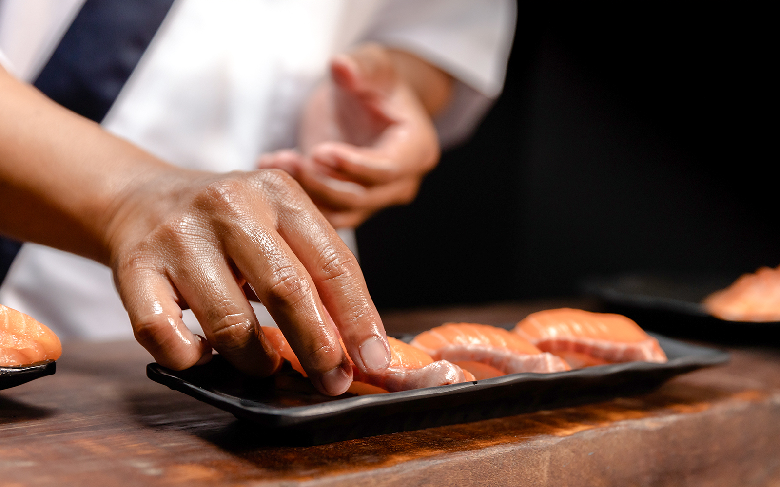 Chef arranging fresh salmon slices on a black plate.