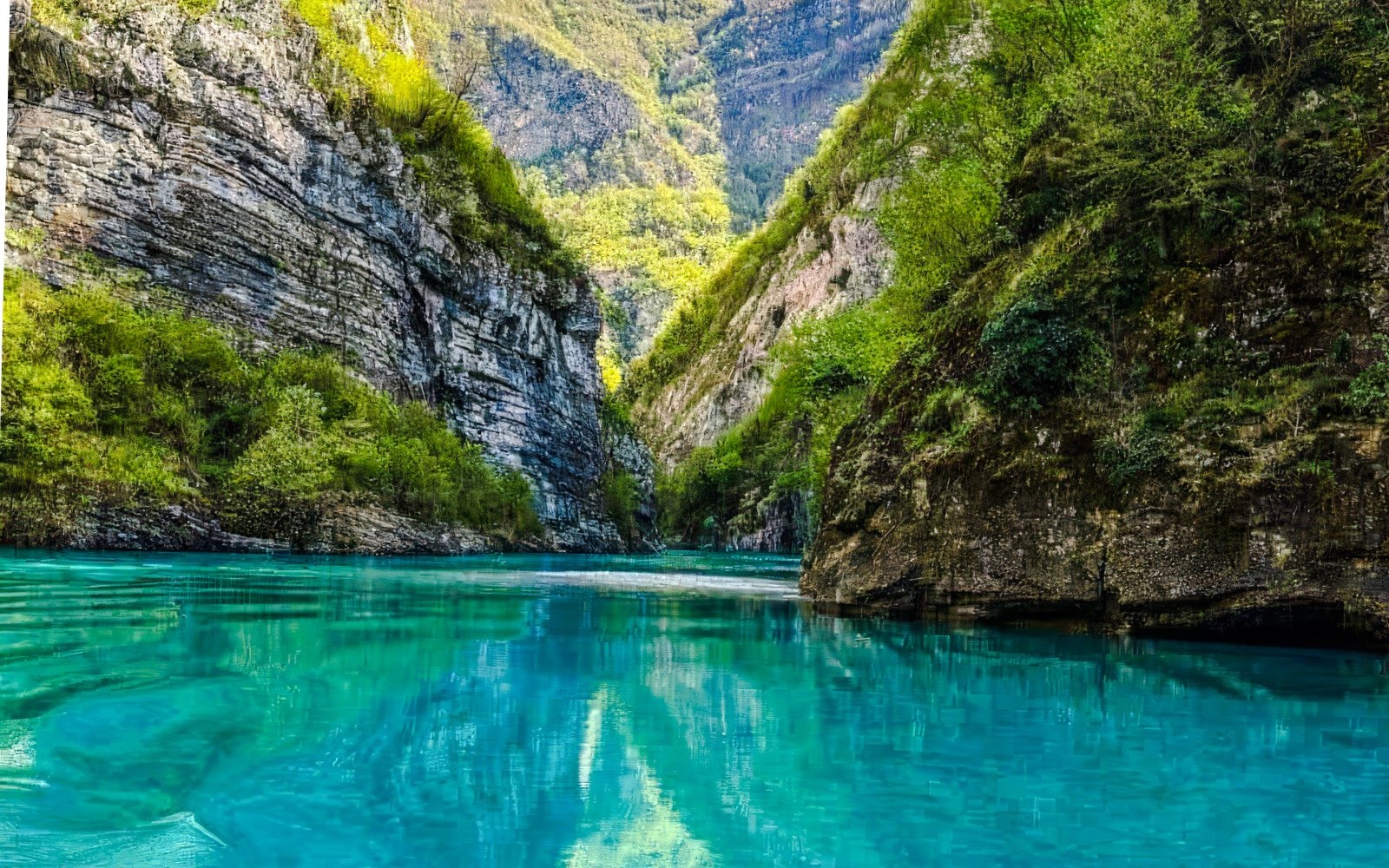 Komani Lake with turquoise water surrounded by steep, lush green cliffs in Albania.