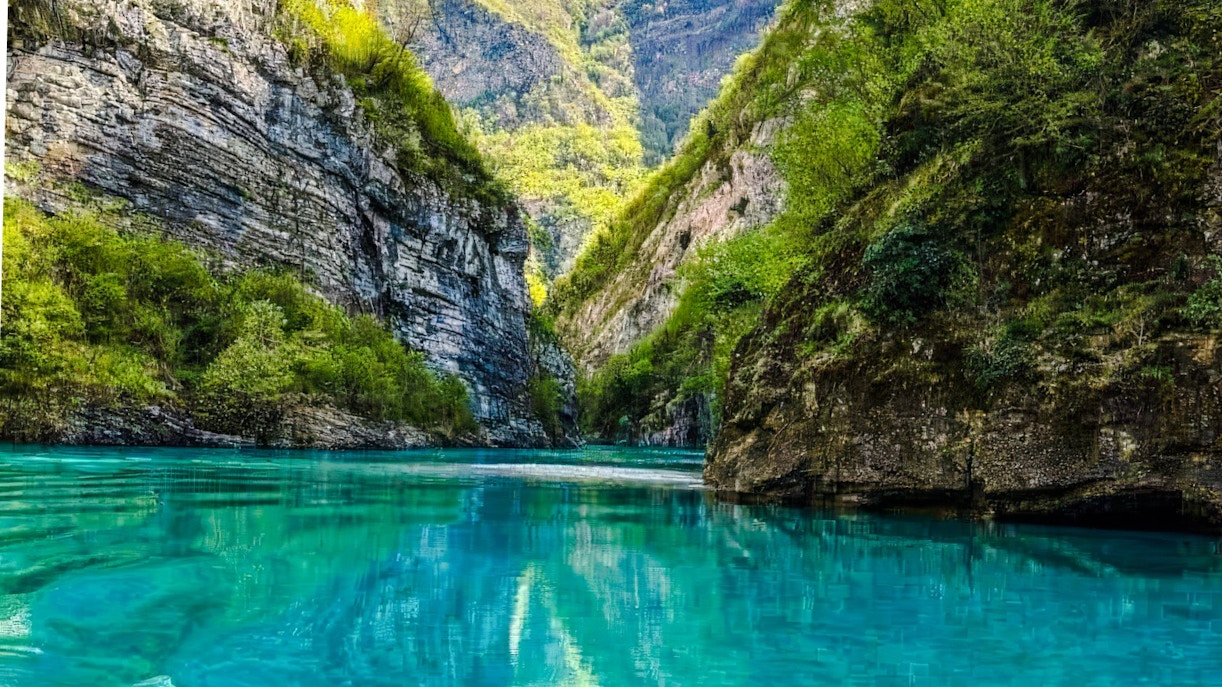 Komani Lake with turquoise water surrounded by steep, lush green cliffs in Albania.
