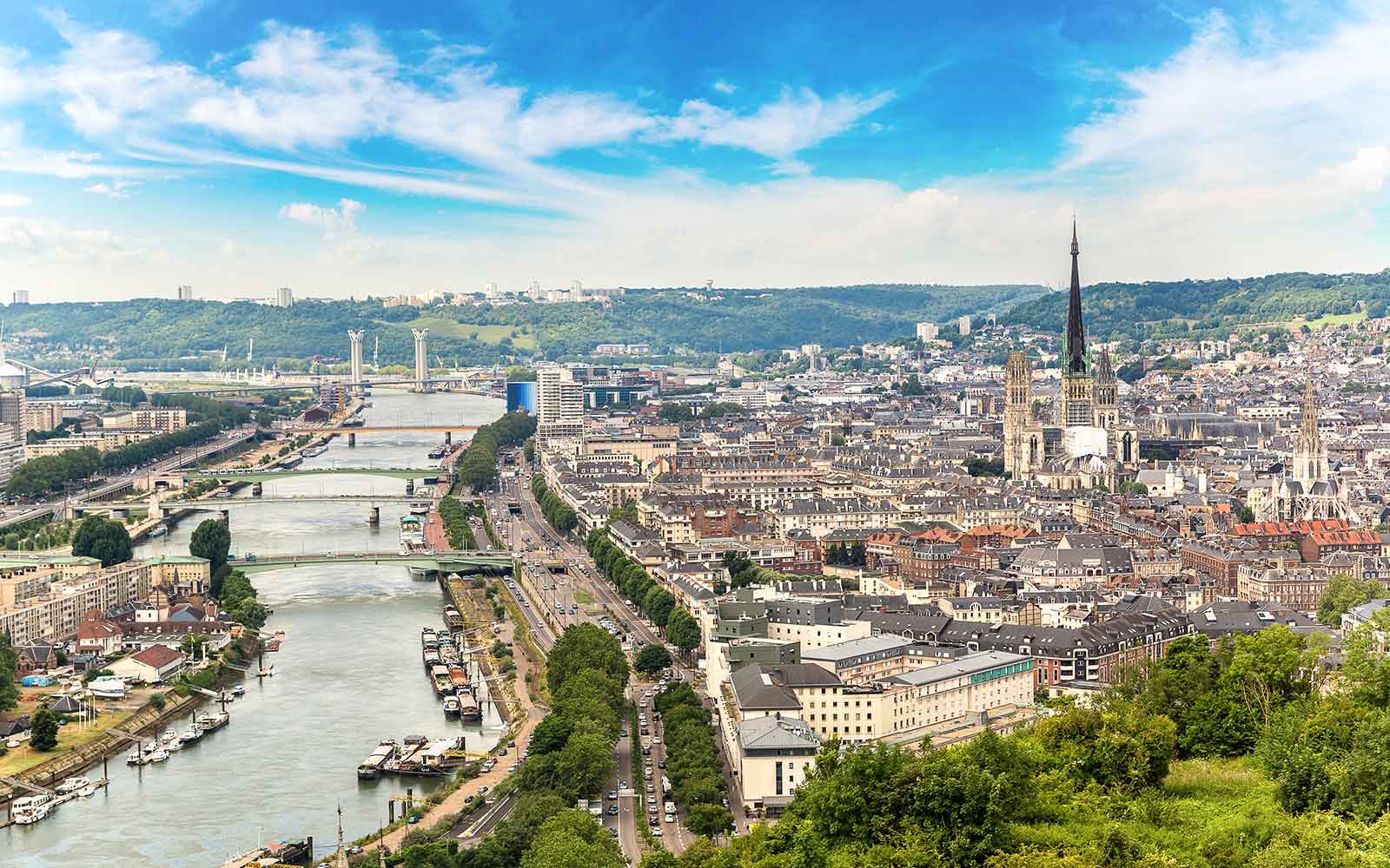 Panoramic view of Rouen with historic buildings and the Seine River in the foreground.