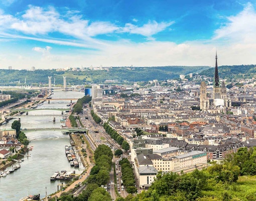 Panoramic view of Rouen with historic buildings and the Seine River in the foreground.