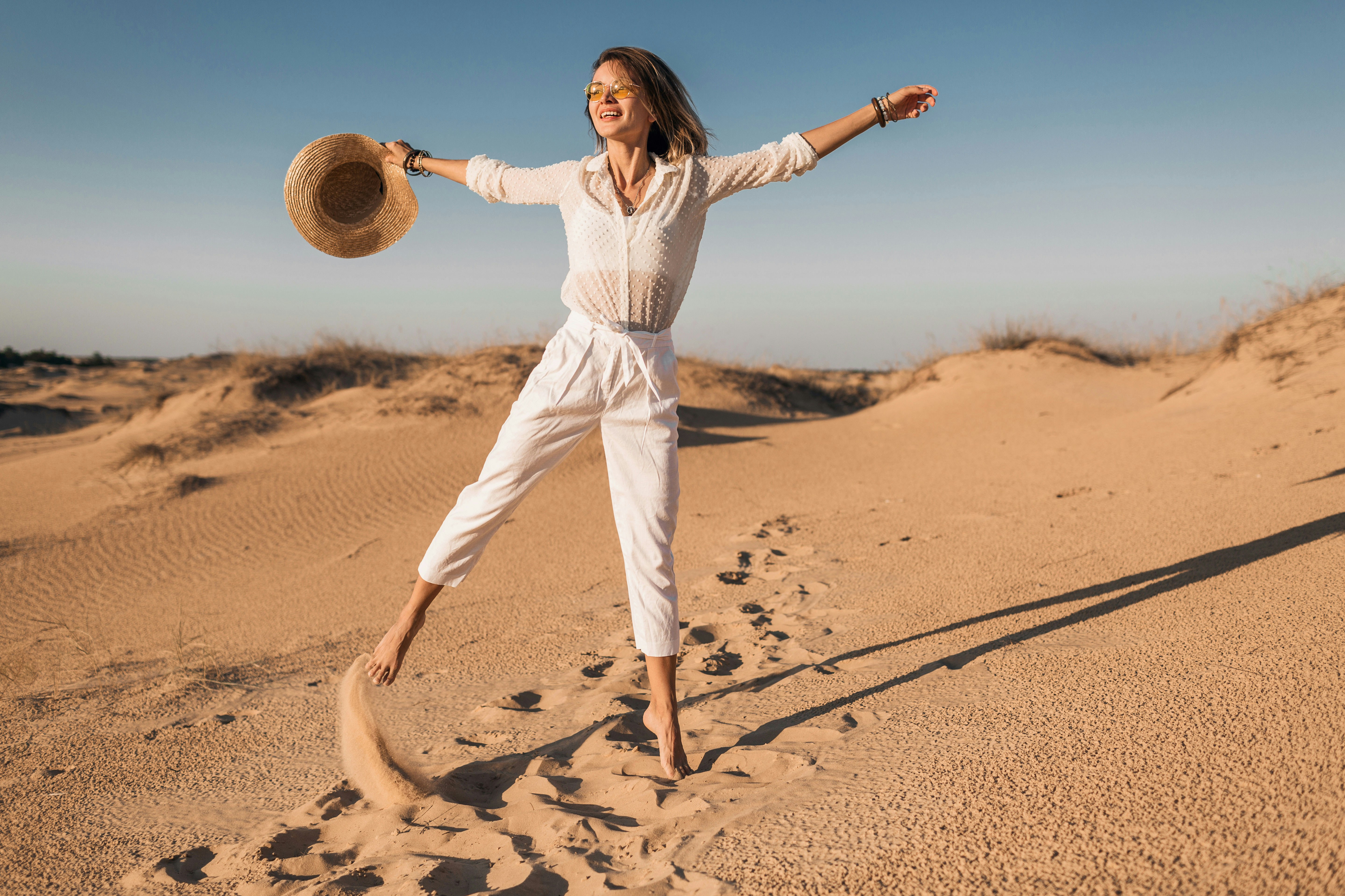 Person enjoying a stroll in a sunny desert, kicking up sand.