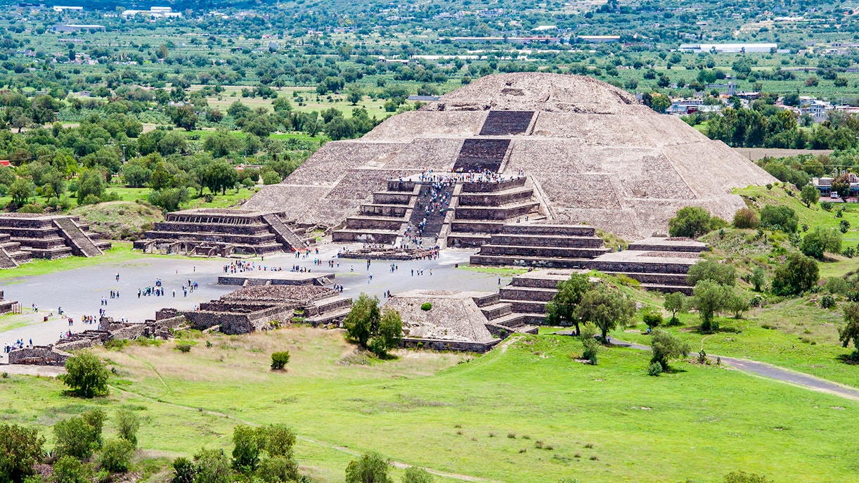 Pyramid of the Moon in Teotihuacan surrounded by trees and tourists exploring.