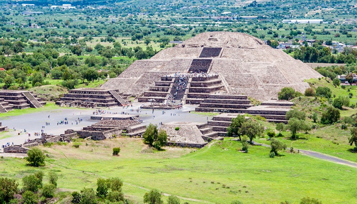 Pyramid of the Moon in Teotihuacan surrounded by trees and tourists exploring.