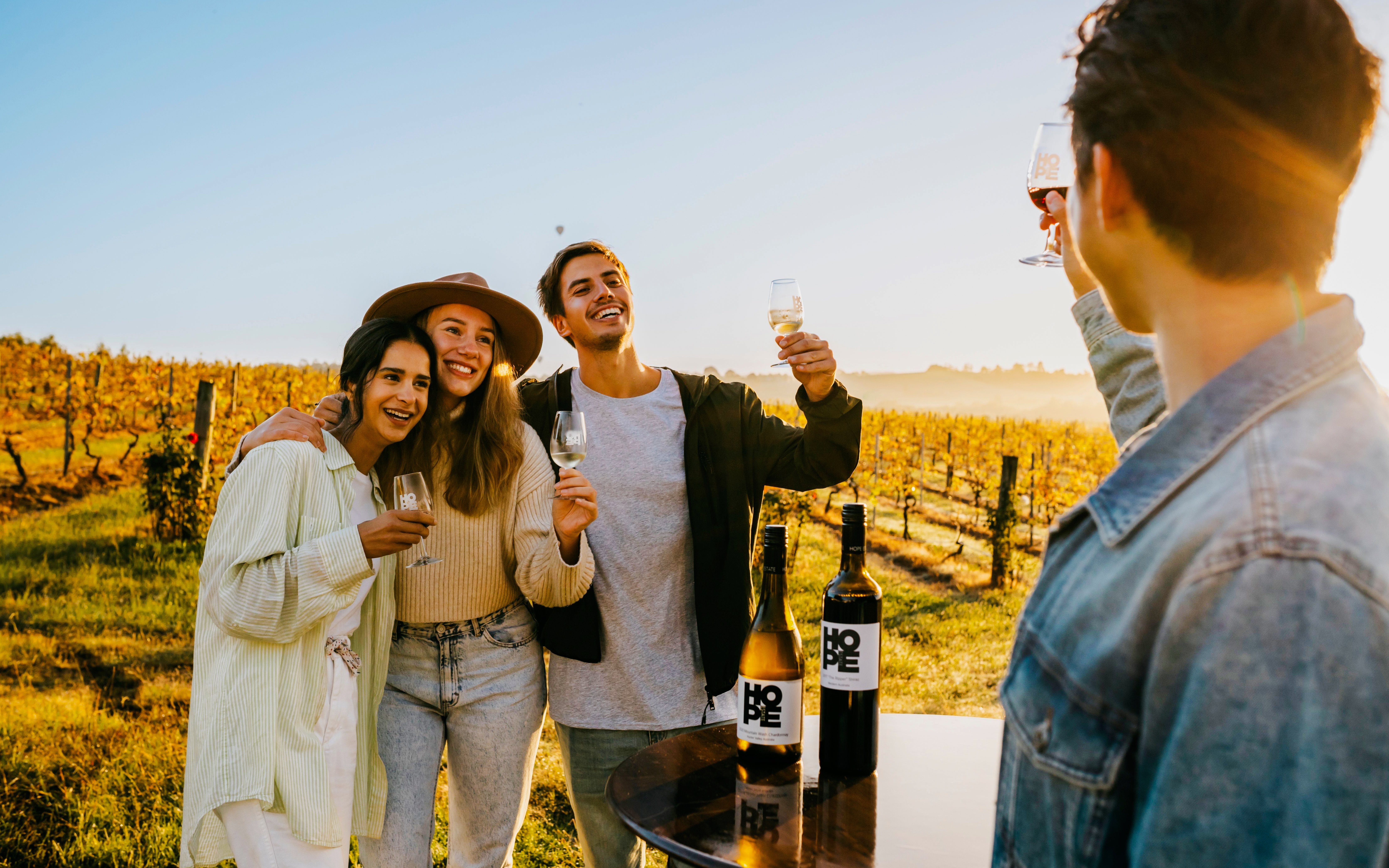 Group enjoying wine tasting at a vineyard estate during sunset.