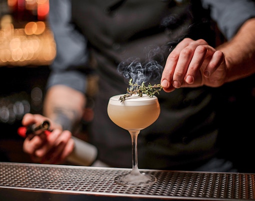 Bartender garnishing a cocktail with herbs at a Singapore bar in October.