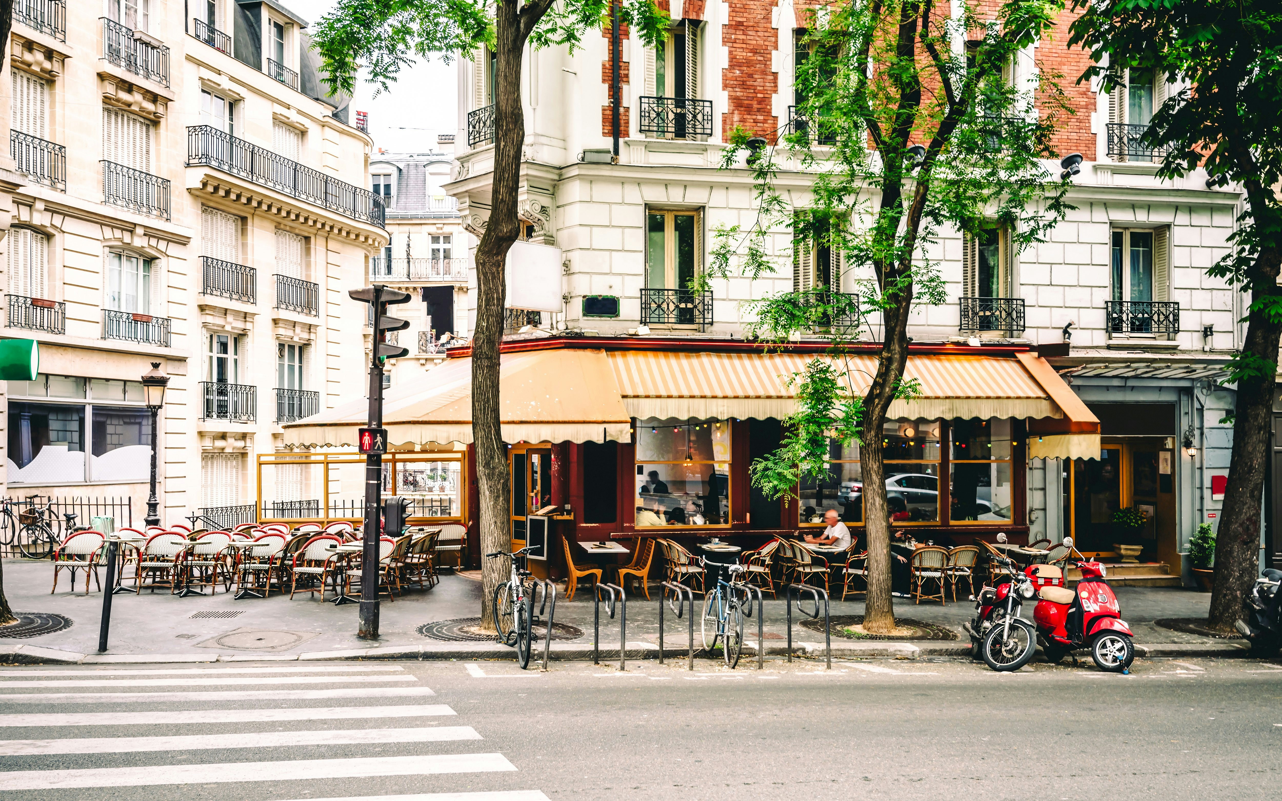 Parisian brasserie with outdoor seating on a tree-lined street corner.