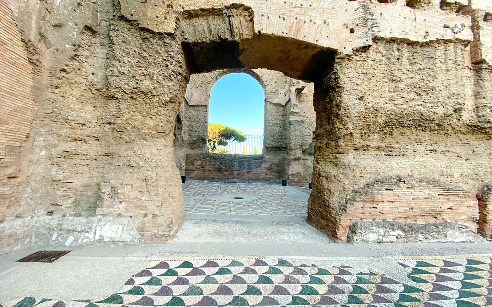 Stone archway at the Baths of Caracalla in Rome, Italy, with mosaic floor and distant trees.