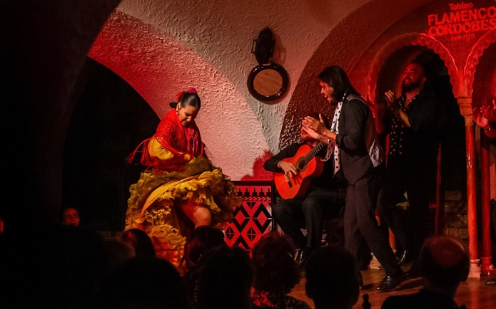 Flamenco dancer performing at Tablao Cordobes with guitarist and clapping audience.