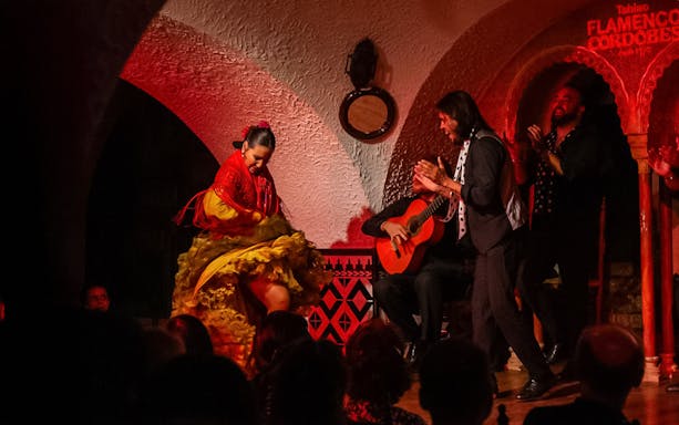 Flamenco dancer performing at Tablao Cordobes with guitarist and clapping audience.