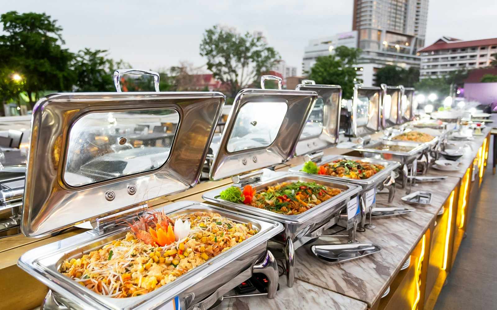 Buffet setup on a cruise ship at Asiatique Pier, Bangkok, with city skyline in the background.