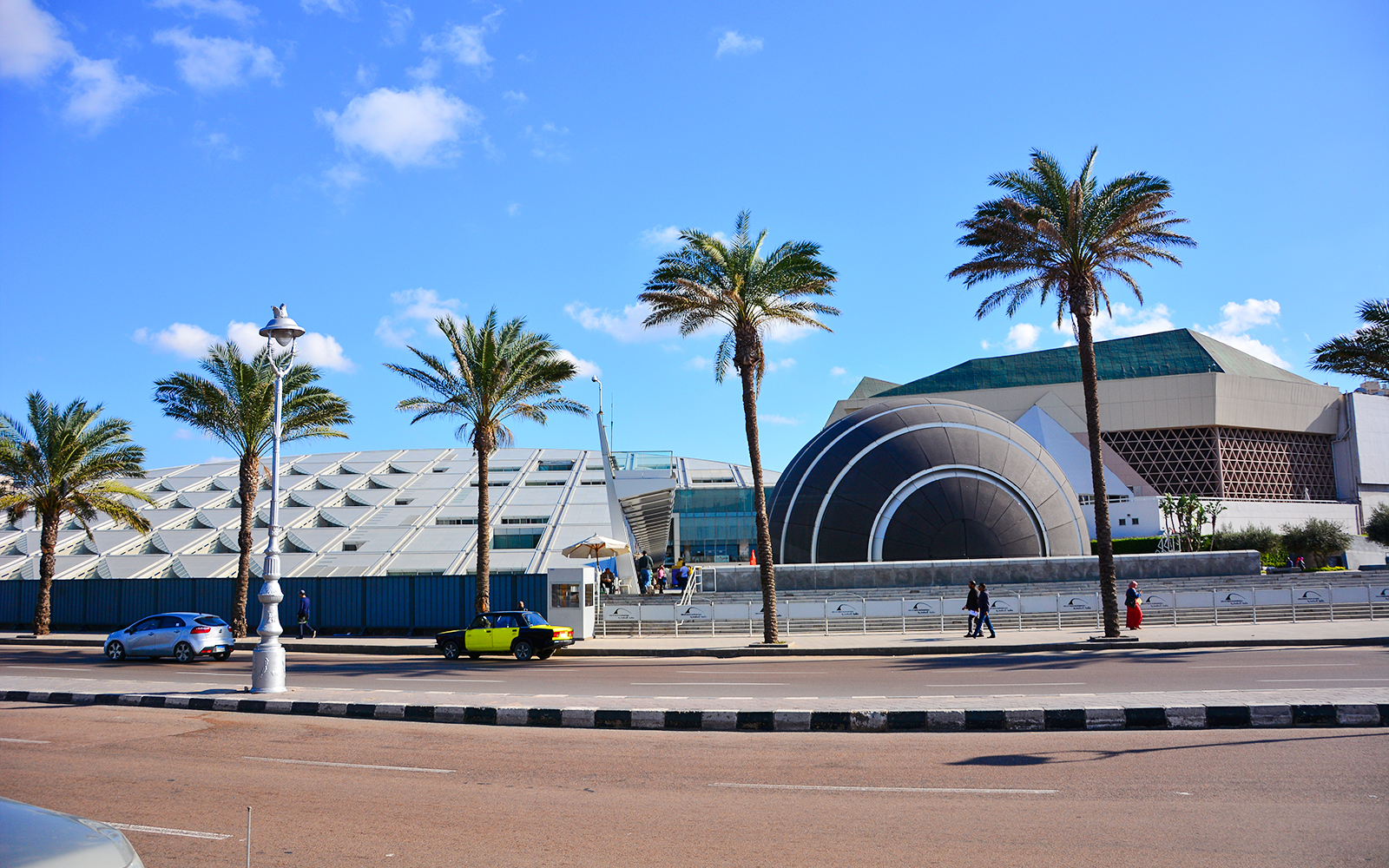 Modern architecture of the Bibliotheca Alexandrina in Cairo, Egypt, with palm trees and street view.