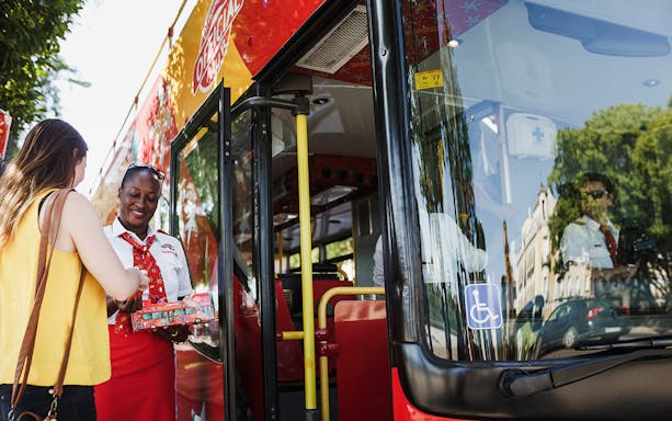 Derry Hop-On-Hop-Off tour bus with a guide assisting a passenger boarding.