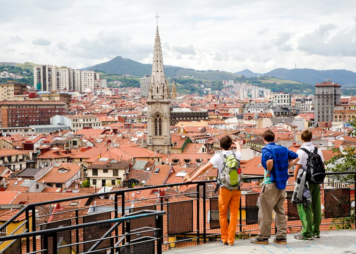 Tourists overlooking Bilbao cityscape with prominent church spire, part of Guggenheim and Gaztelugatxe tour.