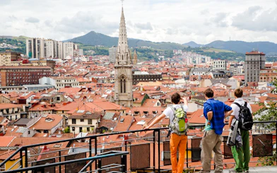 Tourists overlooking Bilbao cityscape with prominent church spire, part of Guggenheim and Gaztelugatxe tour.