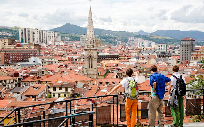 Tourists overlooking Bilbao cityscape with prominent church spire, part of Guggenheim and Gaztelugatxe tour.