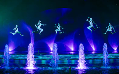 Performers in mid-air during the Kiss of the Sea Show with illuminated fountains.